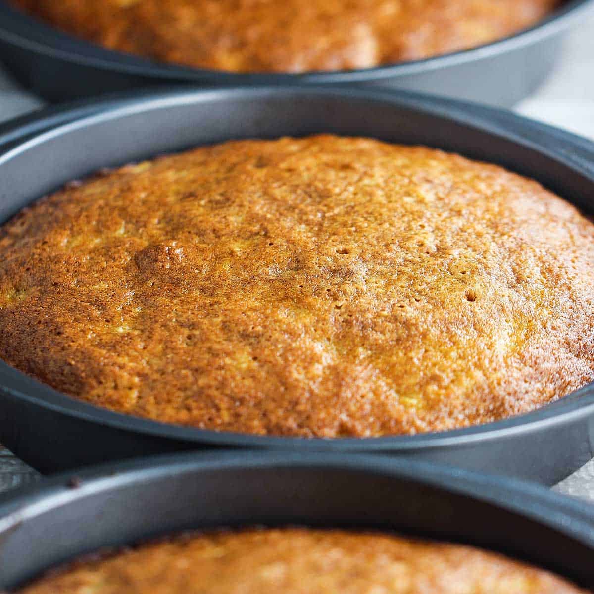 Three cake pans filled with fully cooked carrot cake layers. 