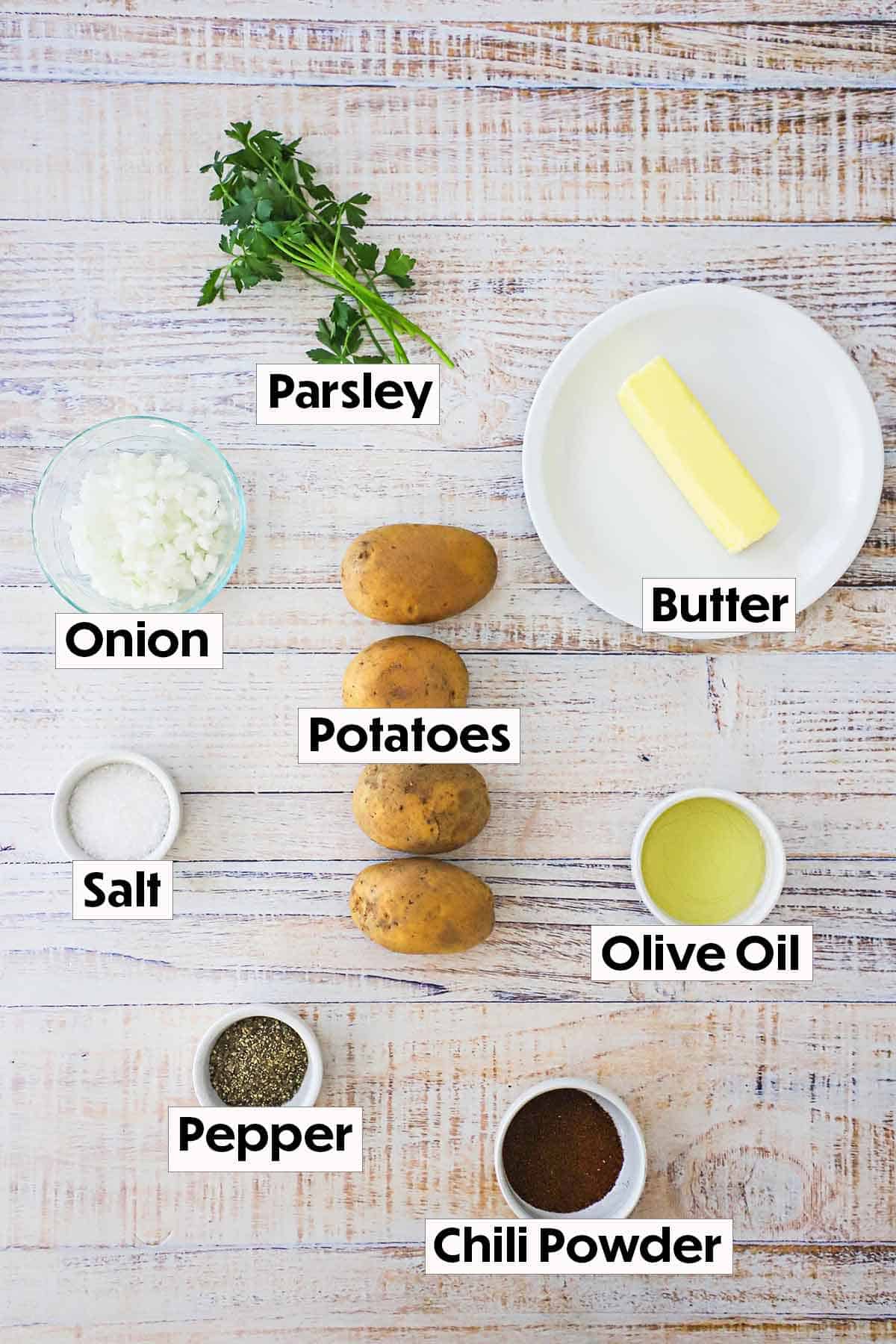 The ingredients for breakfast potatoes including gold potatoes, chopped onion, butter, olive oil, salt, pepper, and parsley arranged on a white background. 