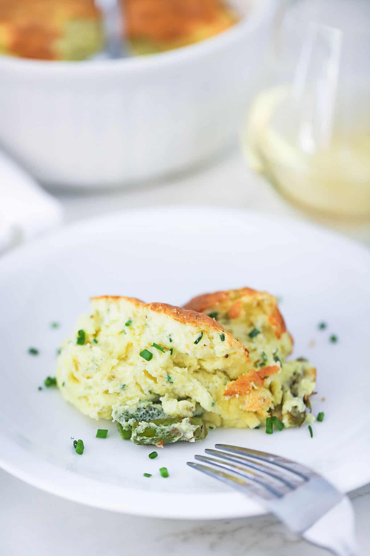 A partially eaten cheese soufflé with asparagus on a white dinner plate with a fork nearby.