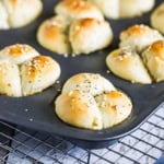 A muffin pan filled with freshly baked cloverleaf dinner rolls resting on a baking rack.