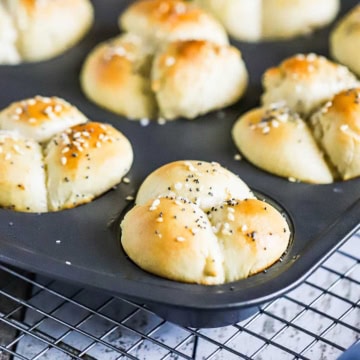 A muffin pan filled with freshly baked cloverleaf dinner rolls resting on a baking rack.