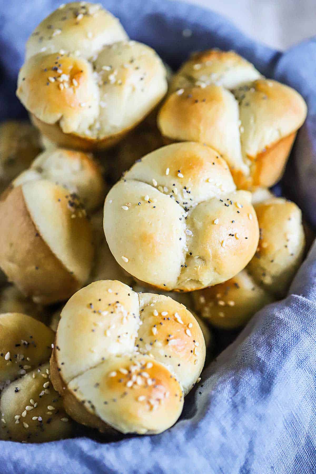 A bread basket lined with a blue linen napkin and filled with cloverleaf dinner rolls. 