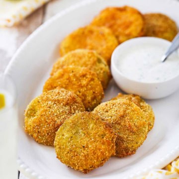 A platter filled with freshly made classic fried green tomatoes with a bowl of Ranch dressing sitting next to them.
