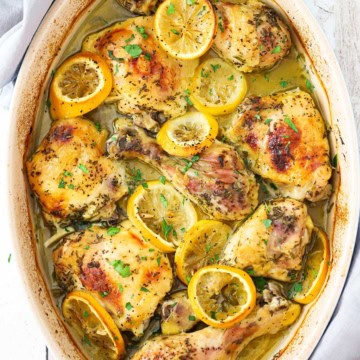 Baked lemon chicken in an oval baking dish topped with roasted slices of lemon and garnished with chopped parsley.