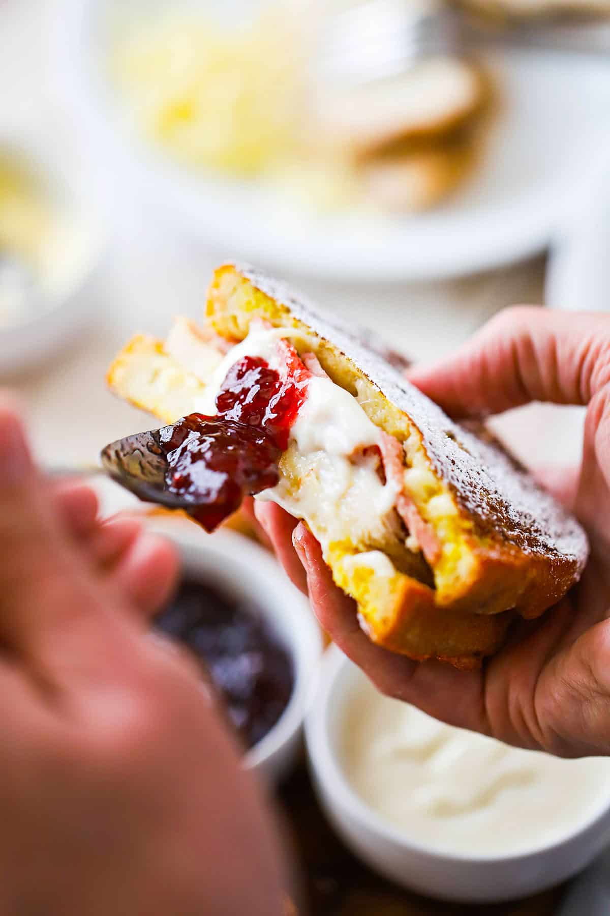 A person smearing fruit preserves onto a Monte Cristo sandwich that has been cut in half.
