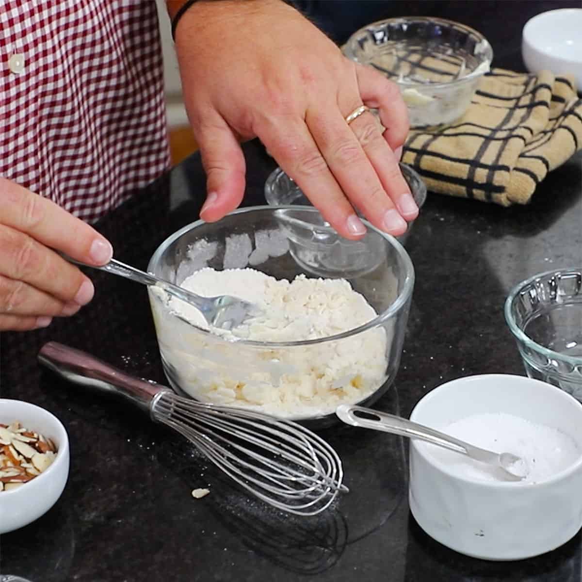 A person using the back of a fork to work softened butter into a flour and salt mixture in a small glass bowl. 