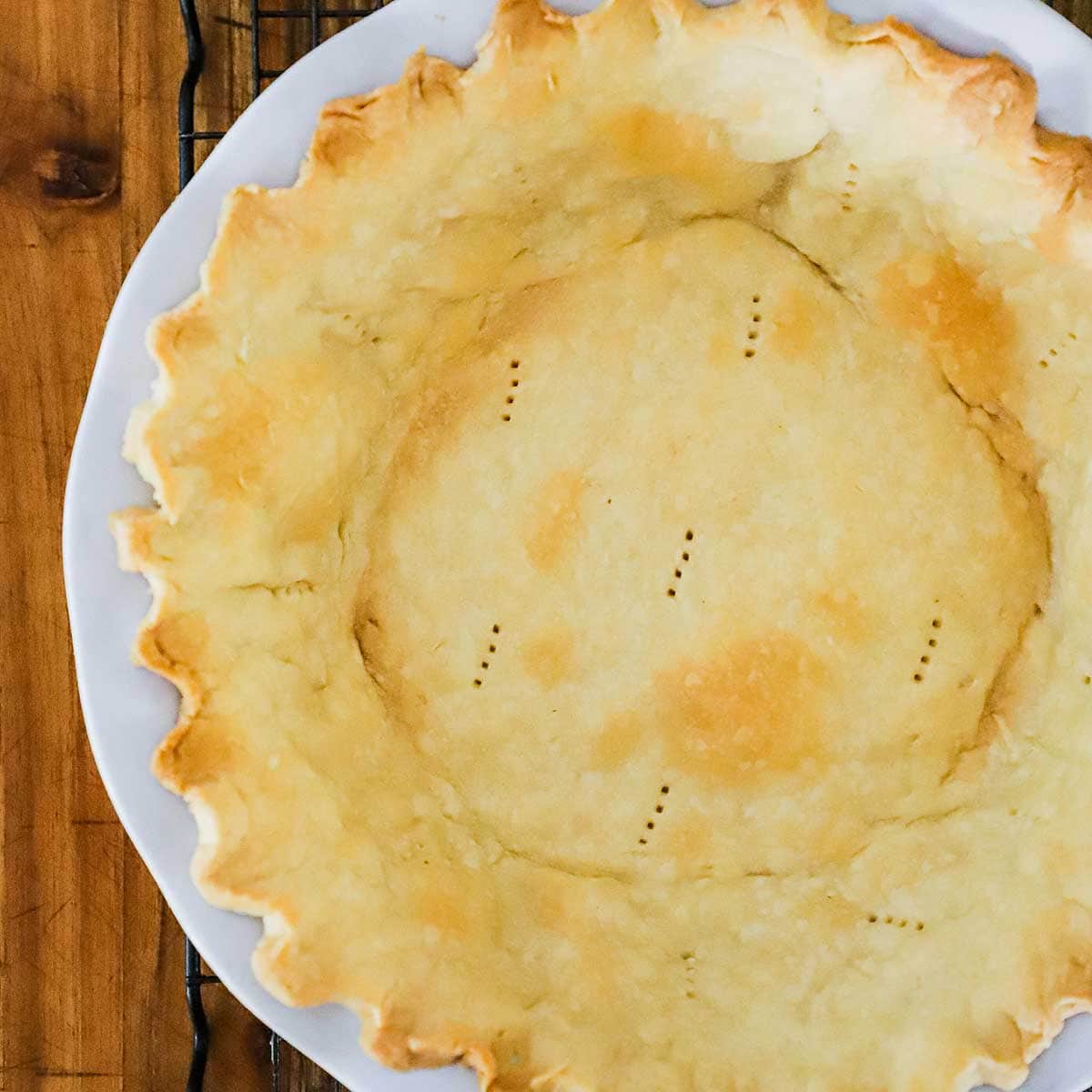 A pie crust that has been par-baked in a white pie dish. 