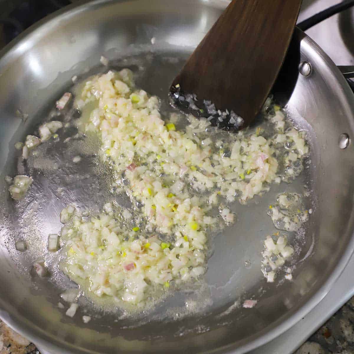 Chopped shallots being sautéed in butter in a large silver skillet.