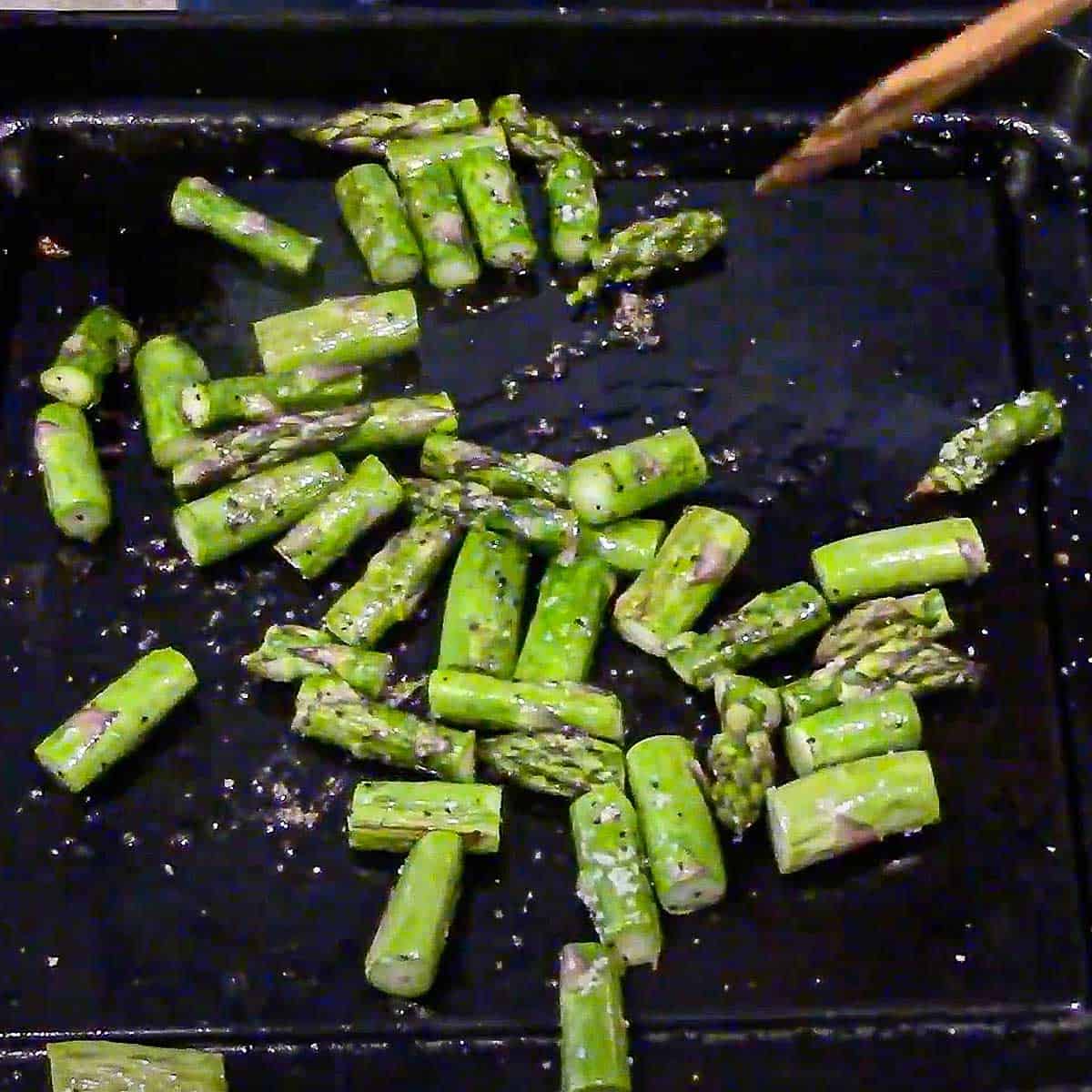 Small pieces of cut asparagus that has been roasted on a small roasting pan and seasoned with salt and pepper.