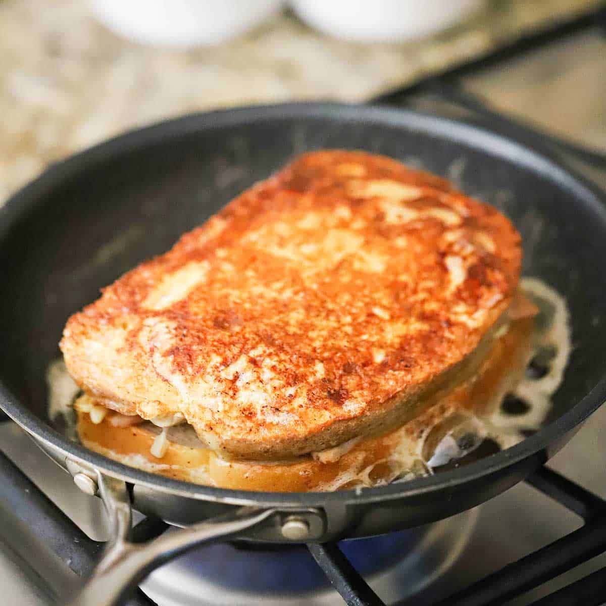 A cooked and lightly browned Monte Cristo sandwich in a skillet filled with simmering melted butter. 