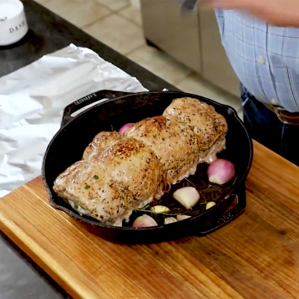 A herb-stuffed pork loin that has been seared and roasted is resting in a cast-iron skillet on a cutting board. 