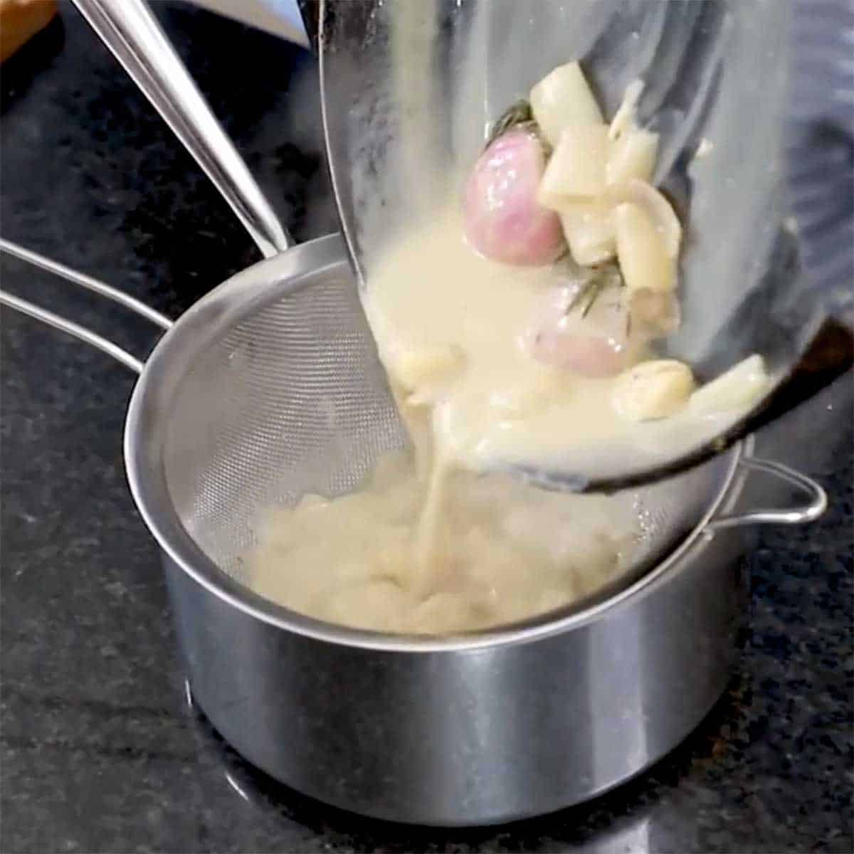 A person straining a sauce through a sieve into a saucepan. 