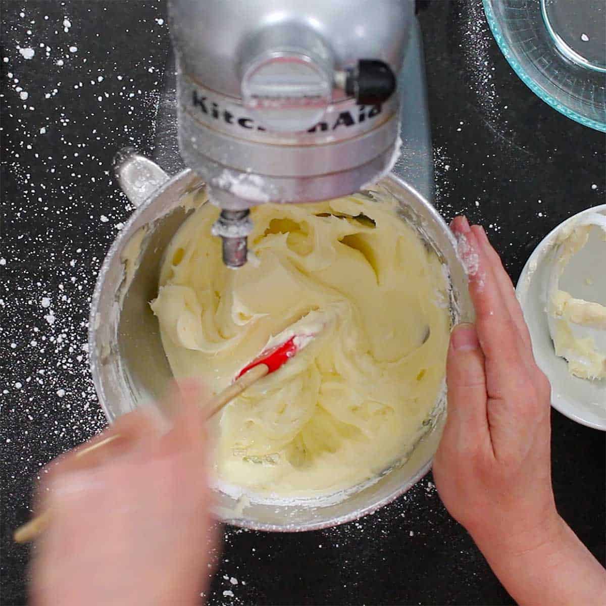 A person using a stand mixer to mix softened cream cheese with softened butter.