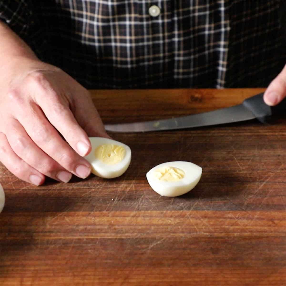 A person using a knife to cut open a hard boiled eggs down the middle, lengthwise. 