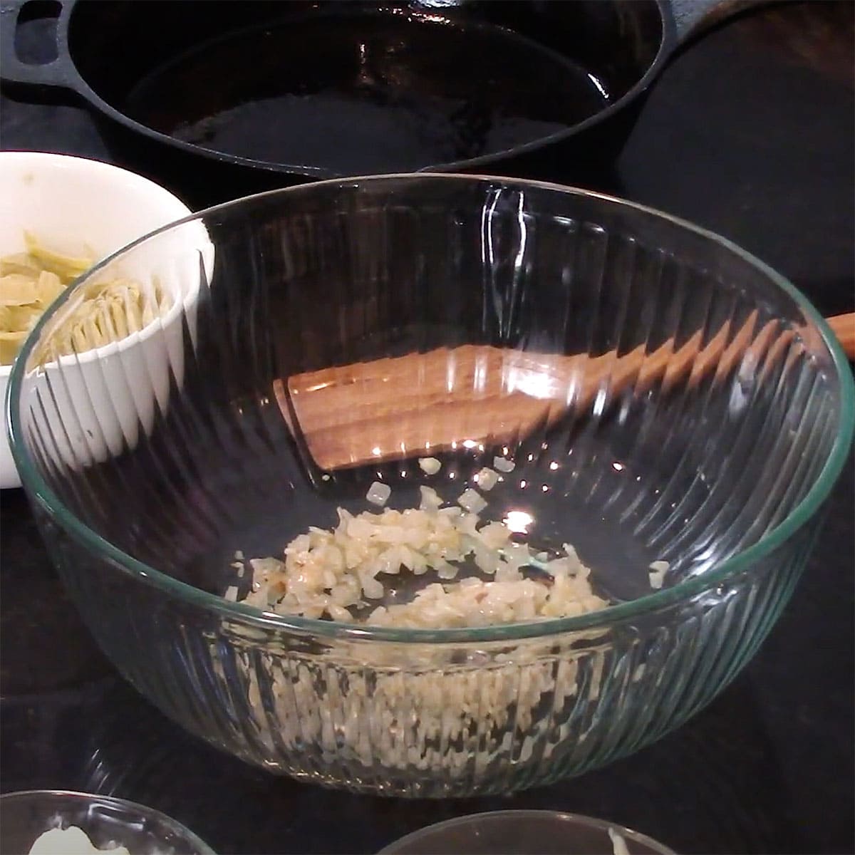 A large glass bowl with about a cup of sautéed onions in the bottom of it.