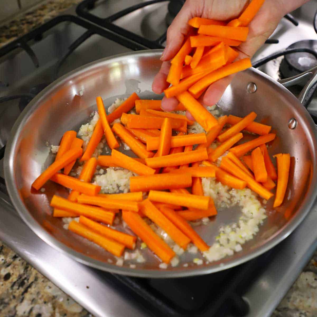 A person adding strips of fresh carrots into a skilet filled with sautéed shallots and simmering butter.