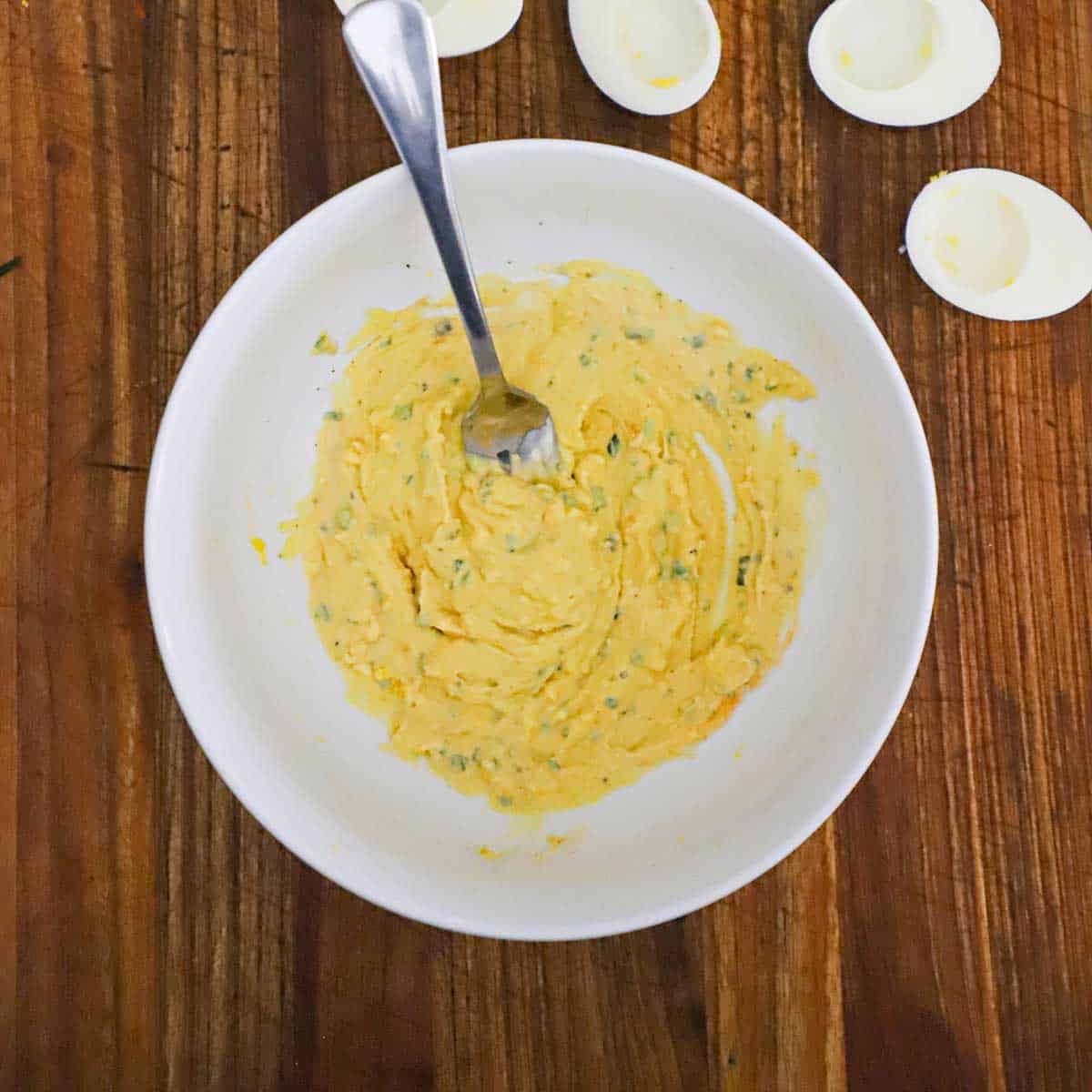 A person using a fork to mash the filling for traditional deviled eggs in a large white bowl. 