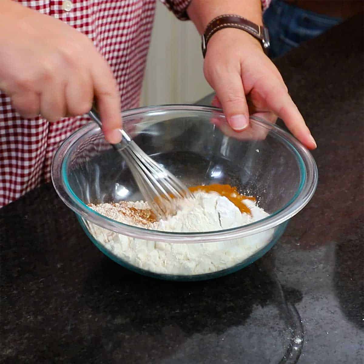 A person whisking flour and cinnamon on a glass bowl. 