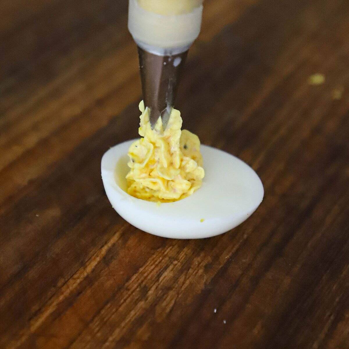 A person piping the ham and cheese filling into a hard boiled egg for ham and cheese deviled eggs. 