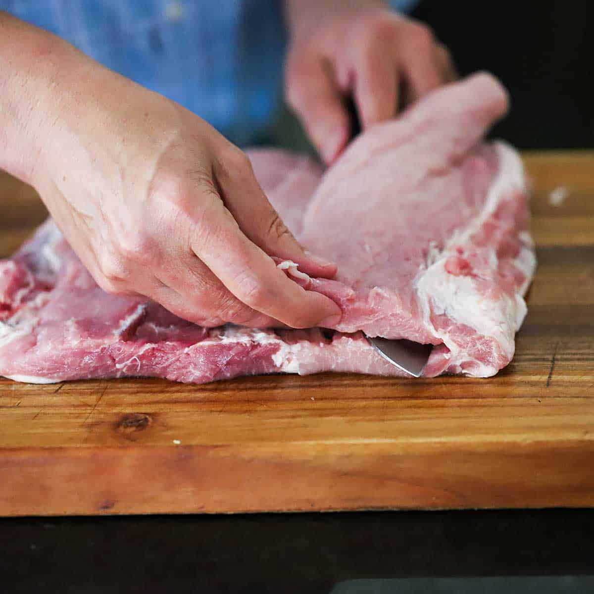 A person using a chef's knife to butterfly and open up an uncooked pork loin. 