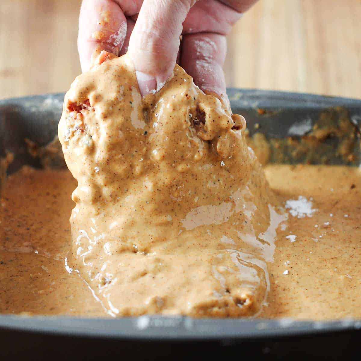 A person dragging a cubed steak through a chicken fried steak batter in a cake pan. 