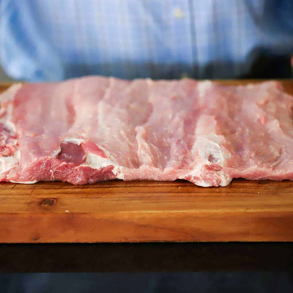 An uncooked pork loin roast that has been butterflied open and is resting on a large cutting board. 