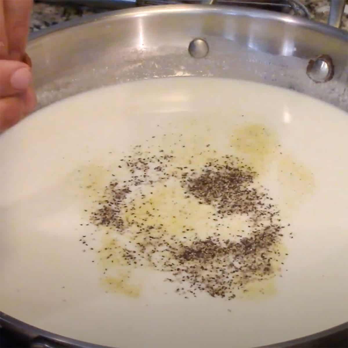 A person sprinkling, salt, pepper, and adobo seasoning in to cream gravy in a large skillet. 