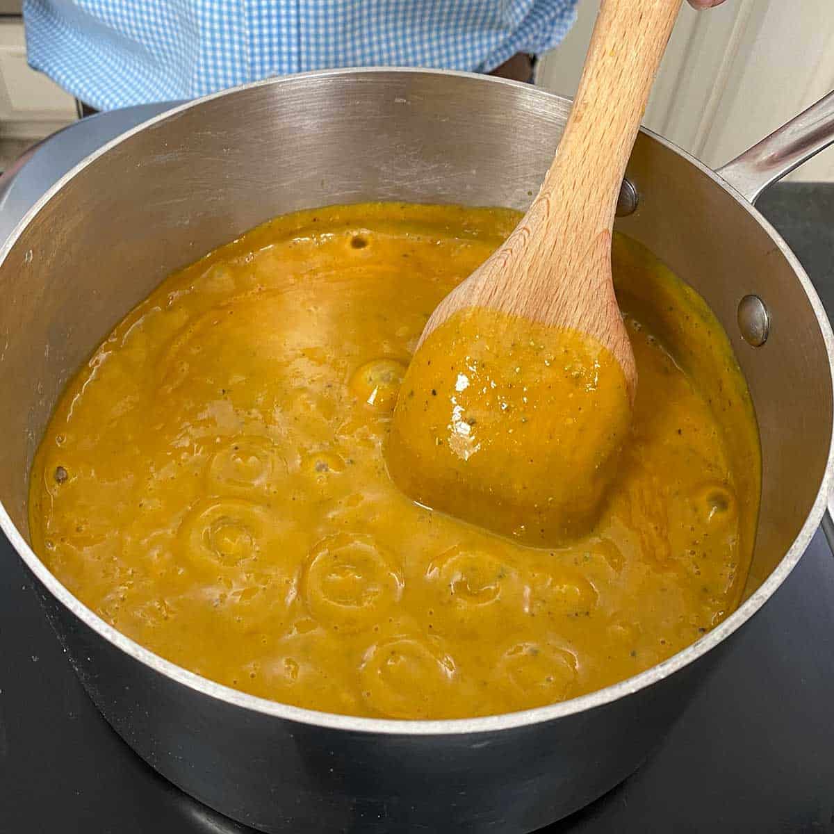 A Carolina mustard sauce simmering in a silver saucepan with a wooden spoon in the middle of the pan in the sauce.