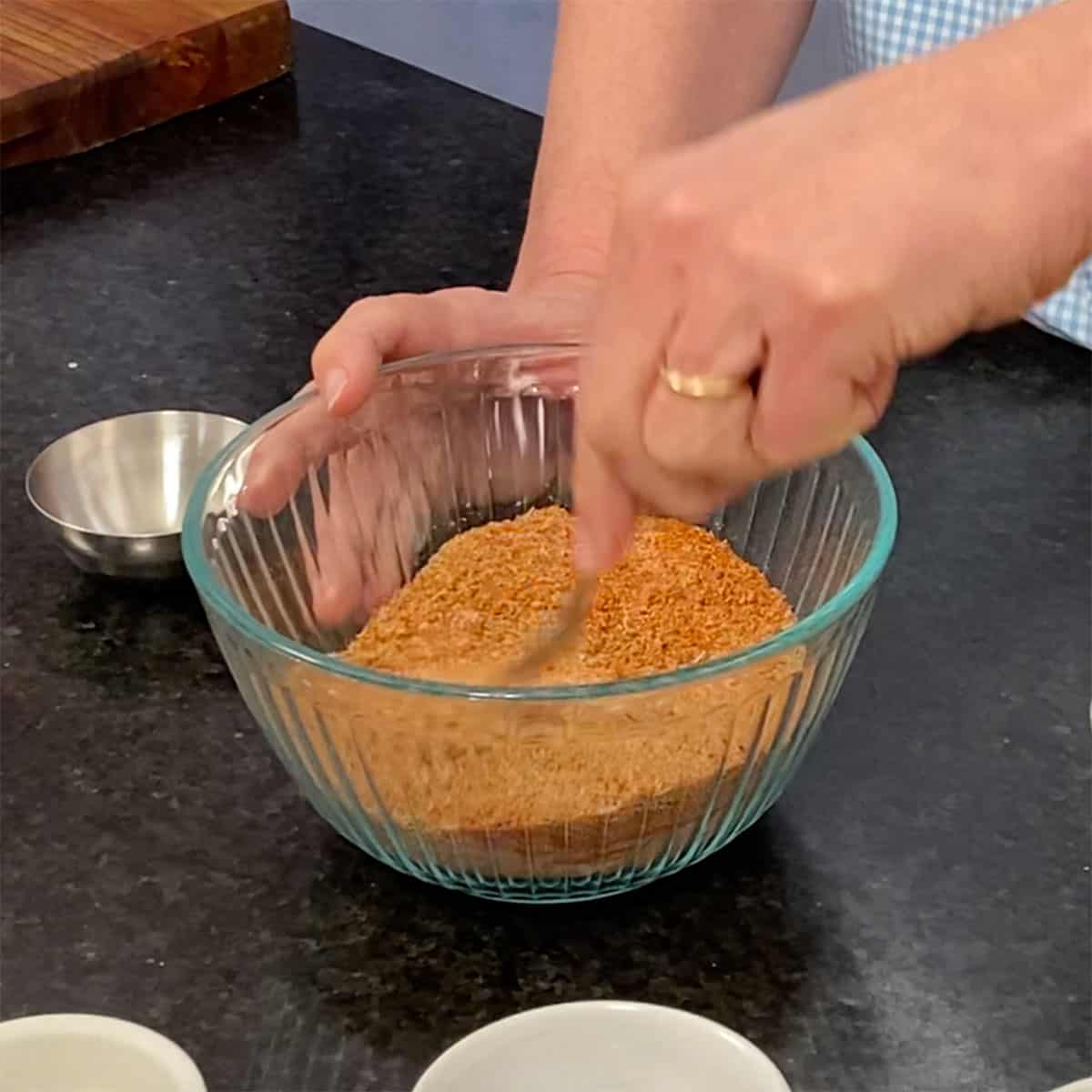 A person using a fork to stir together the dried spices for best pork rub in a glass bowl.