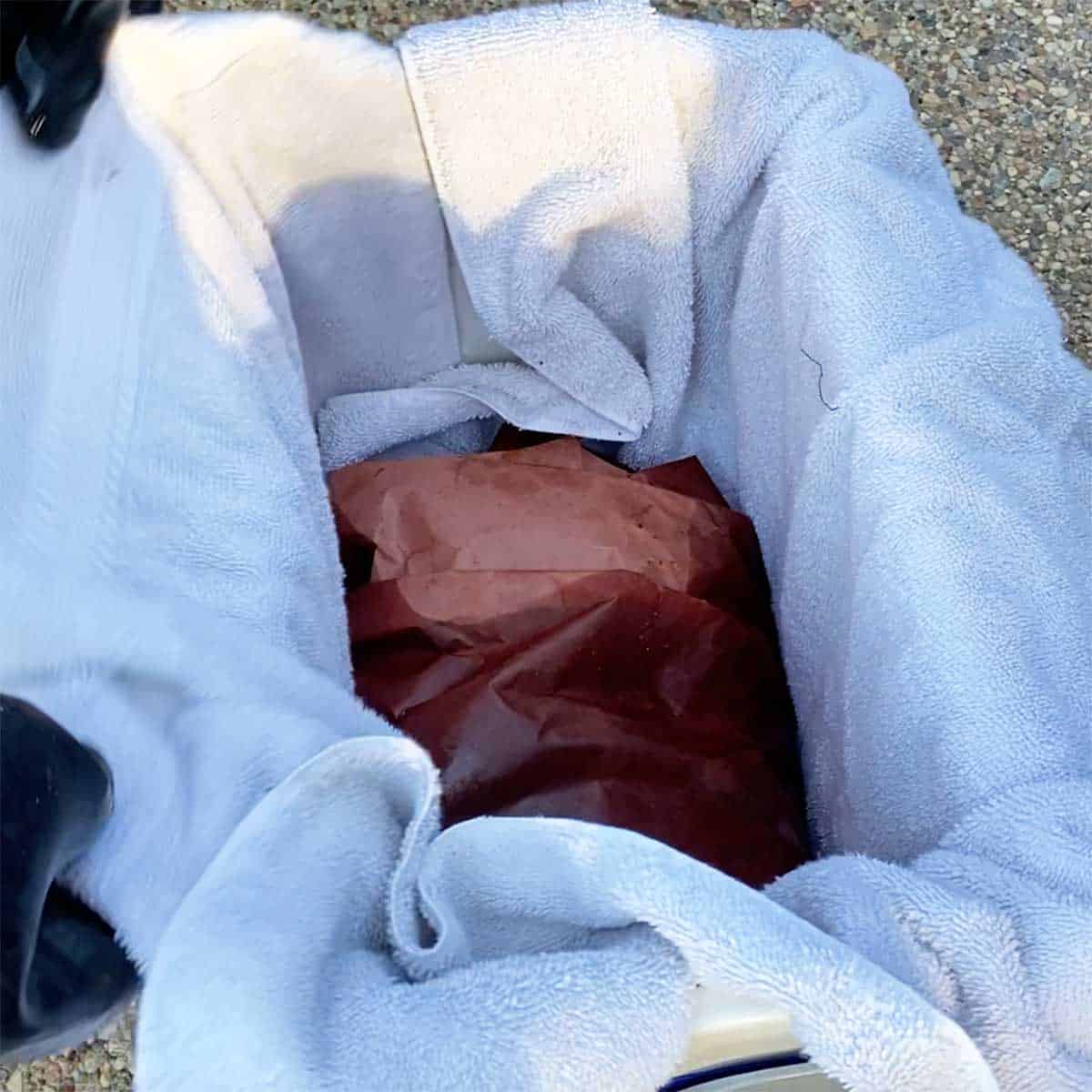 A smoked pork brisket that has been wrapped in pink butcher paper resting in a cooler that has been lined with a bath towel. 
