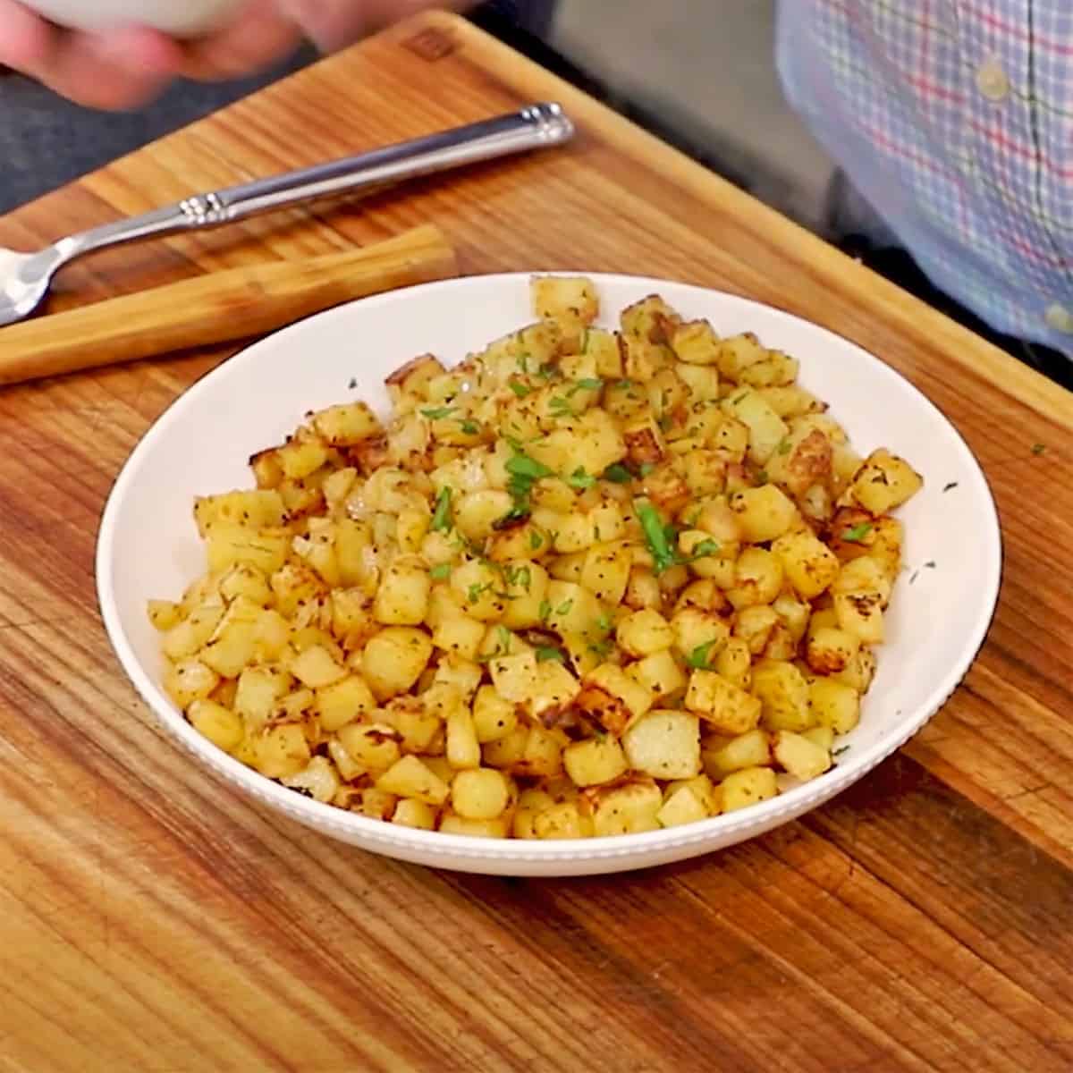A bowl of easy breakfast potatoes in a white bowl on a wooden cutting board. 