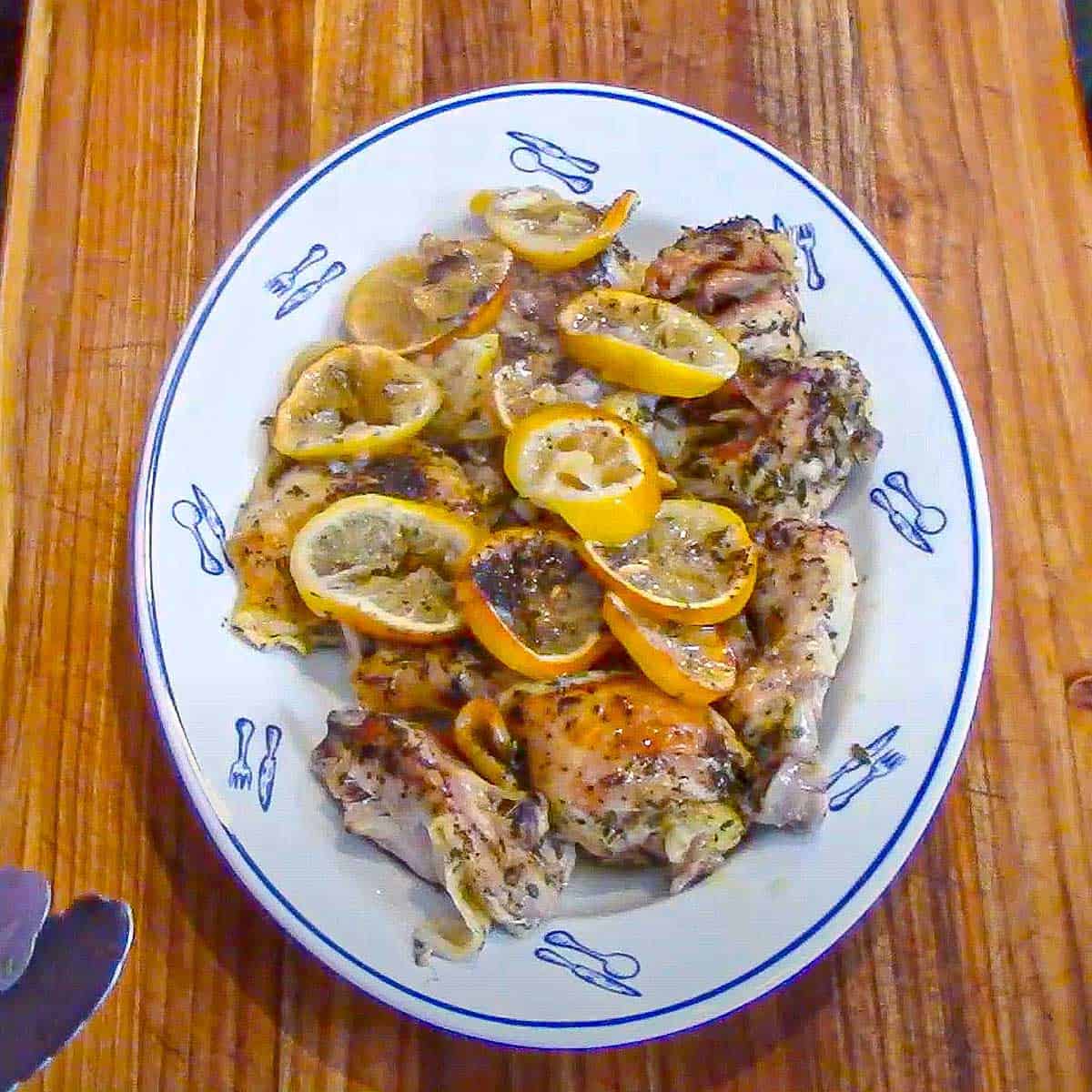 Lemon roast chicken resting on an oval platter topped with slices of roasted lemons.