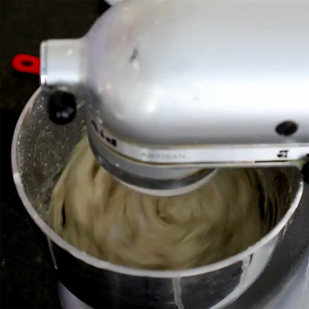 Focaccia dough being kneaded with a dough attachment in a stand mixer. 