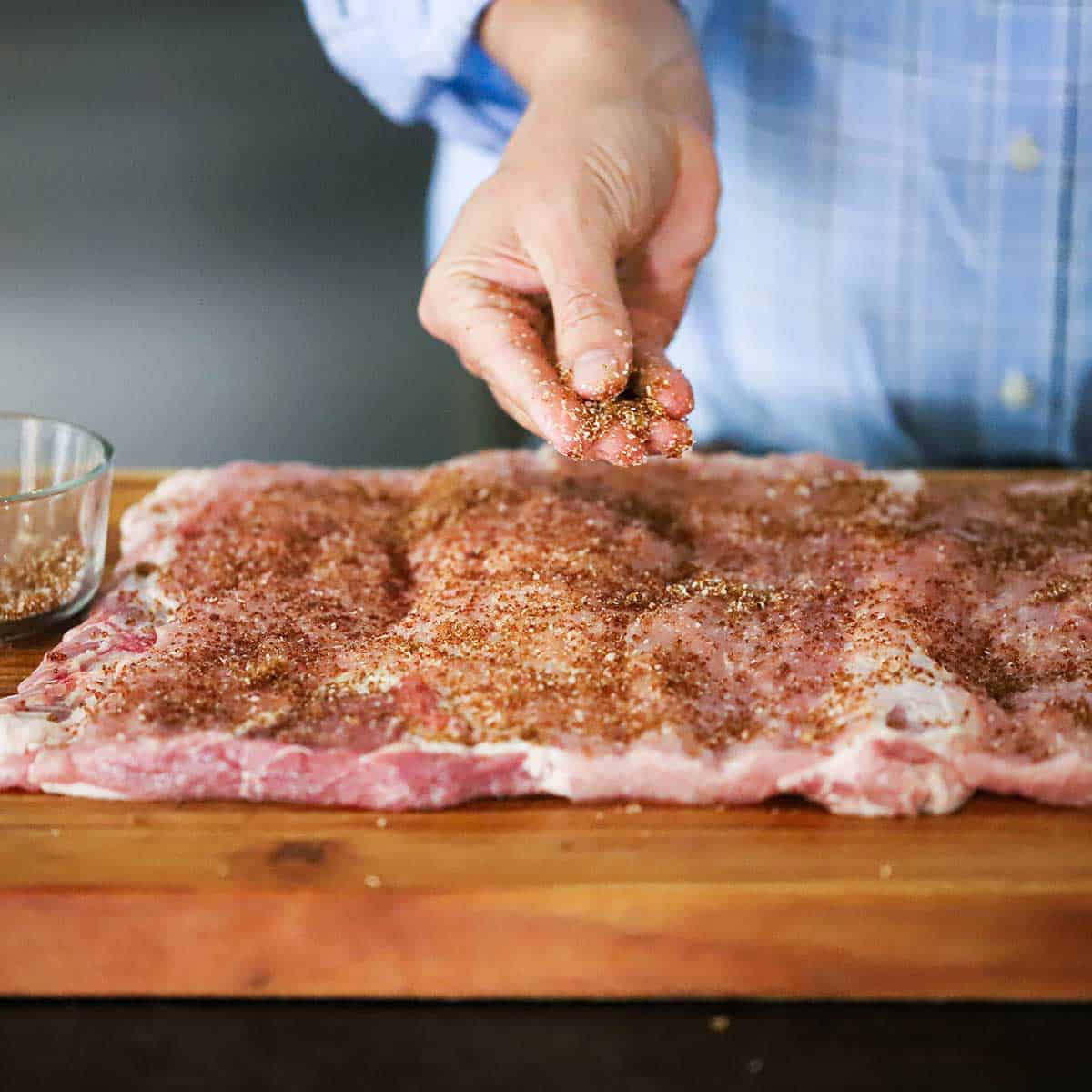 A person sprinkling brown sugar over the surface of an uncooked pork loin that has been butterflied and opened up so it is flat. 