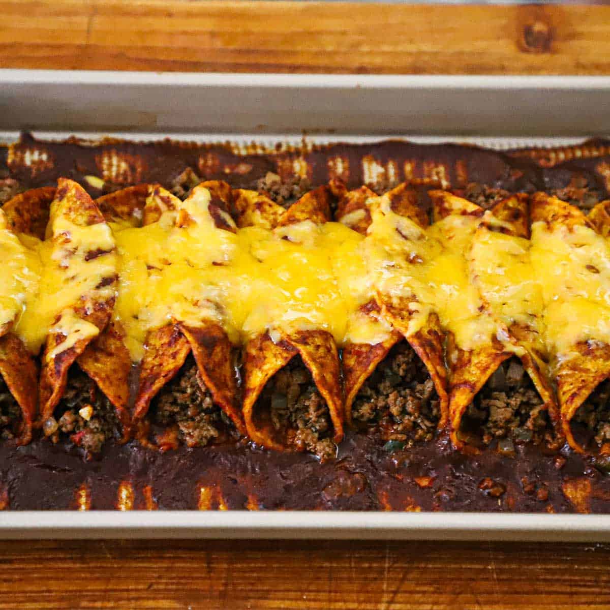 A row of beef enchiladas with red sauce in a sheet pan. 