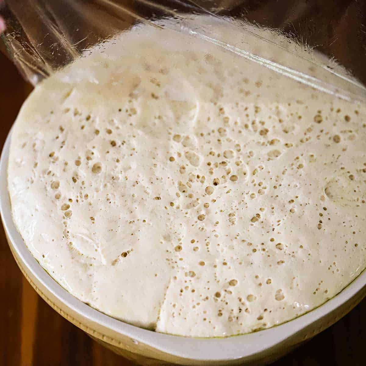 A ceramic bowl that is filled to the top with risen focaccia dough. 