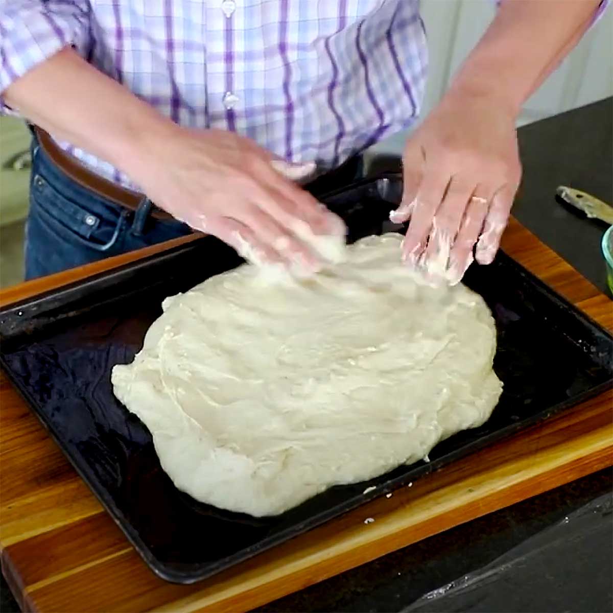 A person spreading focaccia dough onto a baking sheet pan. 