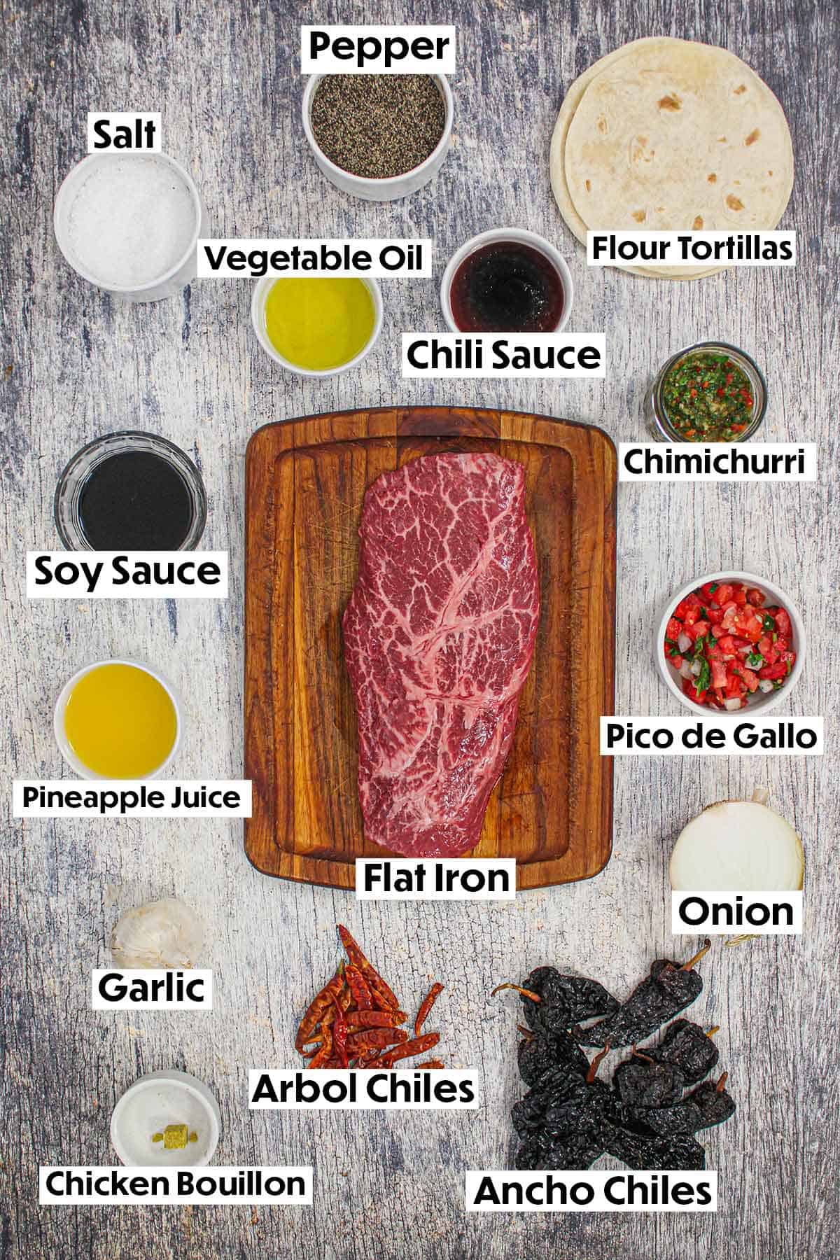 A collection of ingredients on a wooden background for grilled carne asada including steak, tortillas, chiles, pineapple juice, spices, soy sauce, and pico de gallo.