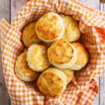 A pile of Southern buttermilk biscuits in a basket lined with a orange and white checkered cloth napkin.
