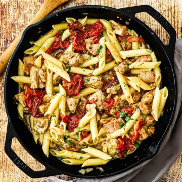A large cast-iron skillet filled with pasta with roasted tomatoes and pesto chicken.