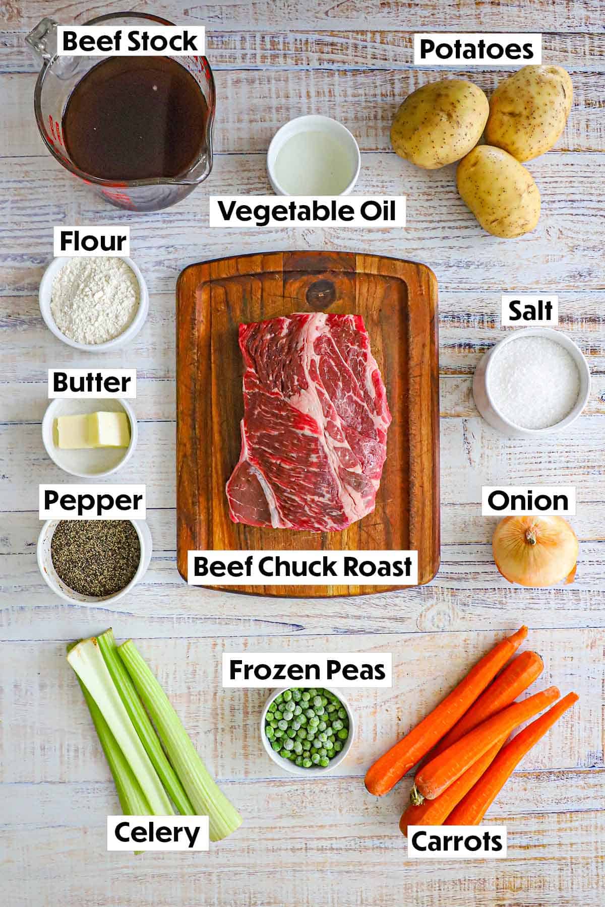 An arrangement of ingredients for classic pot roast on a white background including a beef chuck roast, stock, celery, potatoes, carrots, onion, seasonings, flour, and oil.