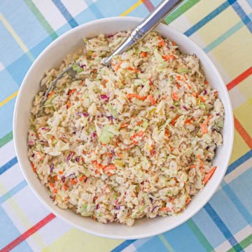 An overhead view of a bowl of diner-style coleslaw with a serving spoon inserted into the side of the dish.