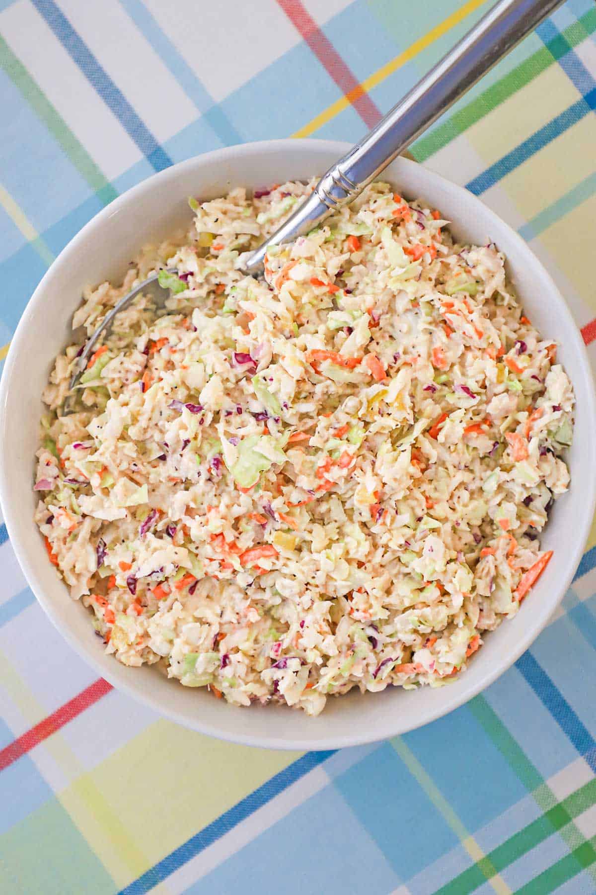 An overhead view of a bowl of diner-style coleslaw with a serving spoon inserted into the side of the dish.