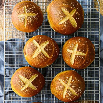 An overhead view of six homemade pretzel buns resting on a wire baking rack.