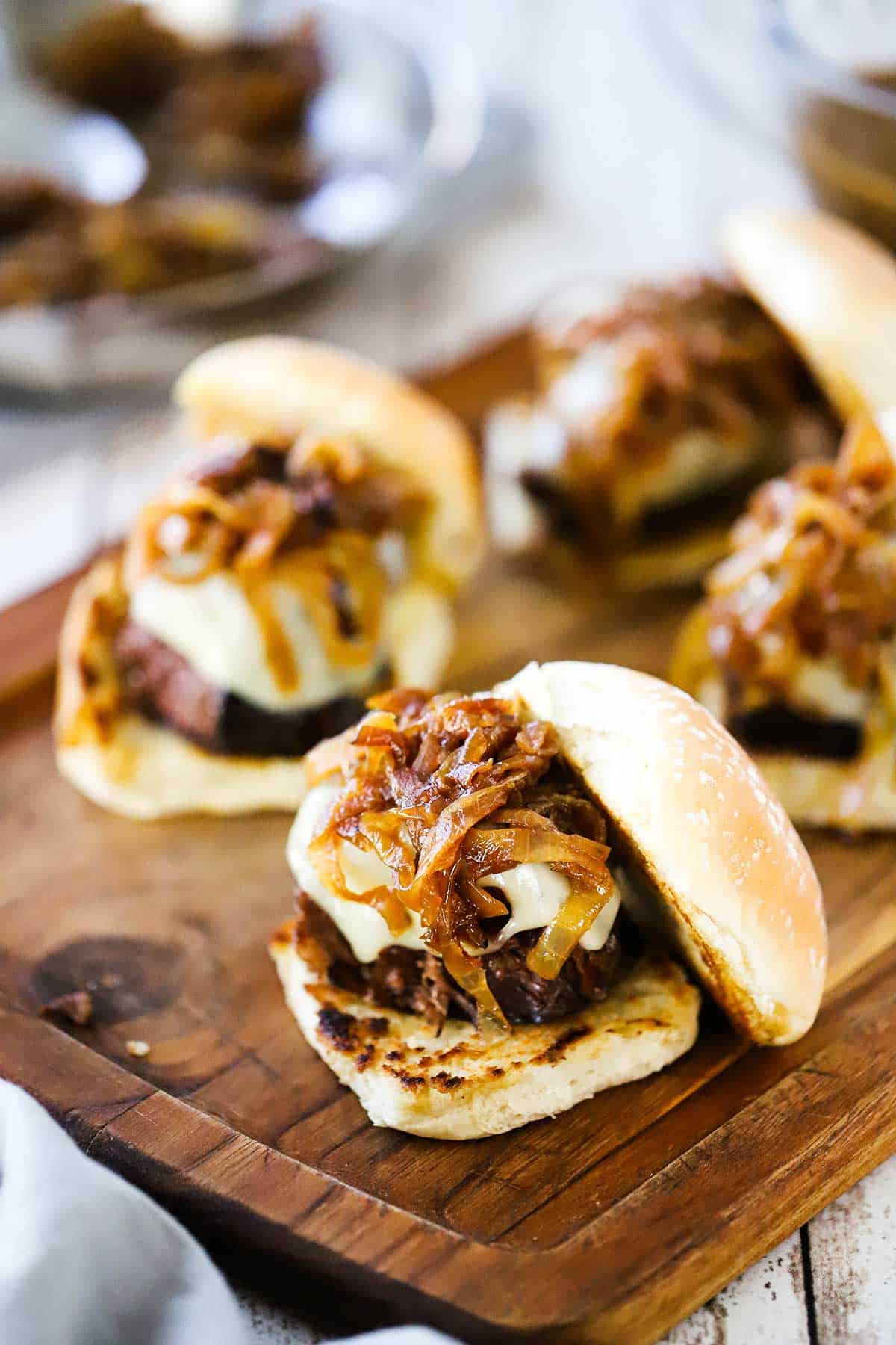 Two rows of pot roast sliders on toasted slider buns with the cooked pot roast topped with Swiss cheese and caramelized onions.