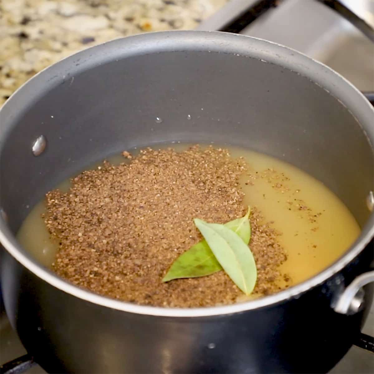 A saucepan filled with turkey stock, water, seasonings, and bay leaves.