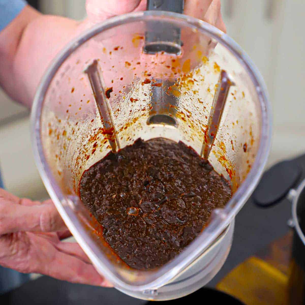 A person holding the pitcher of a blender with puréed chiles and seasonings in it.