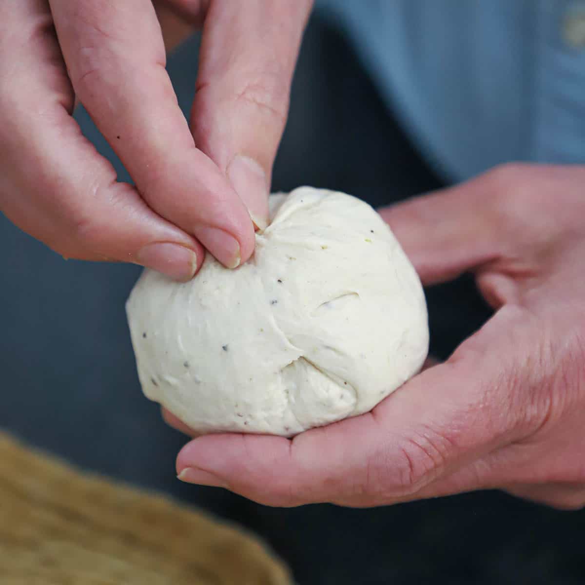 A person using his fingers to form bagel dough into a taut ball.