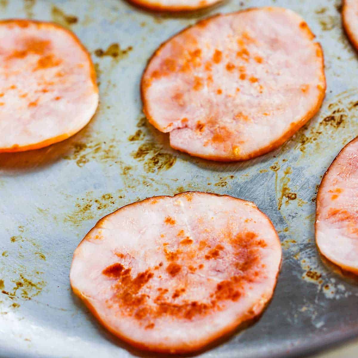 Several slices of seared Canadian bacon in a silver skillet.