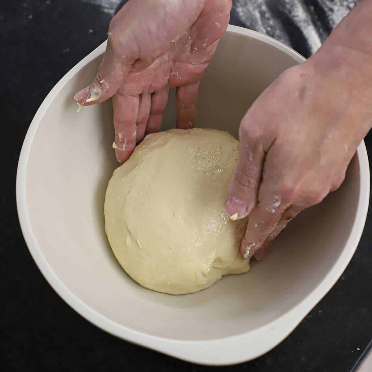 A person turning a ball of pizza dough in a grease ceramic bowl.